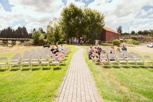 Outdoor wedding ceremony setup with brick pathway leading to altar surrounded by white chairs on green lawn.