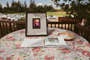 A wedding reception setup with floral tablecloth and wooden benches in a rustic outdoor venue with trees in the background.