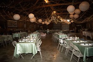 Rustic barn wedding reception setup with white round paper lanterns, twinkle lights, and elegant table settings.