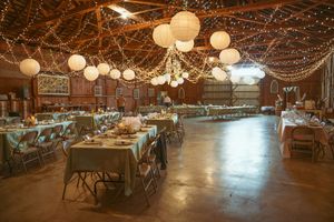 Wedding reception venue with rustic decor featuring round paper lanterns and wooden tables in a barn-style setting.