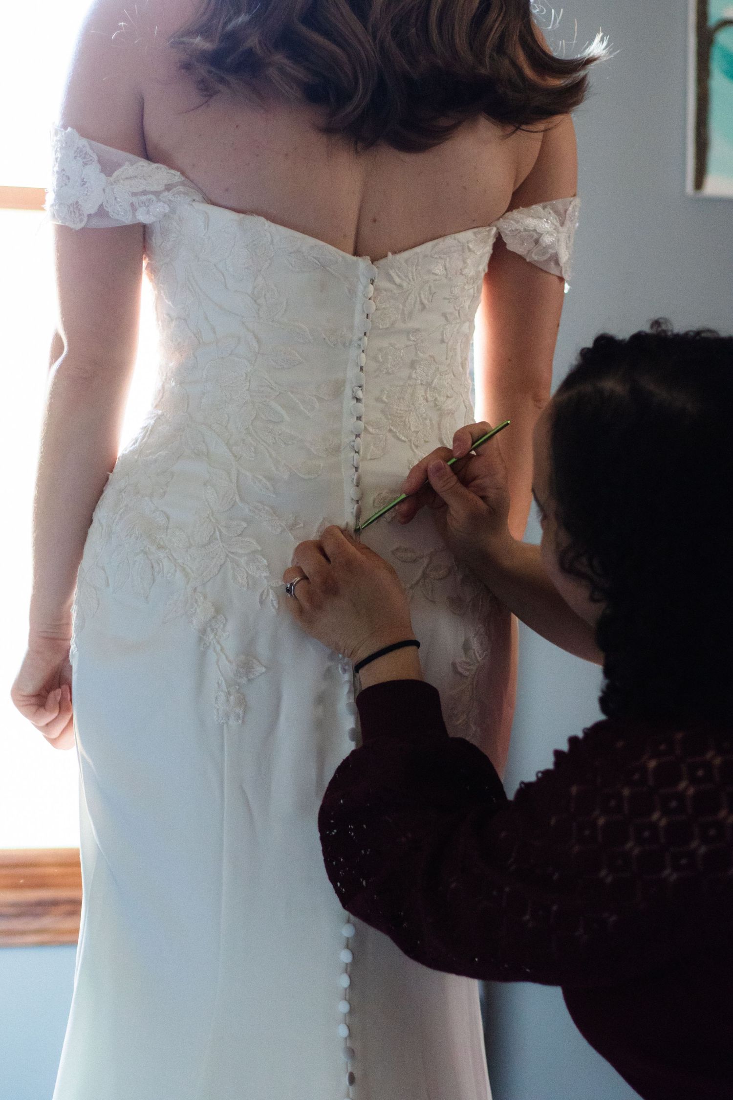 Bride's sister hooking up the lace of her floral lace bridal gown before intimate wedding