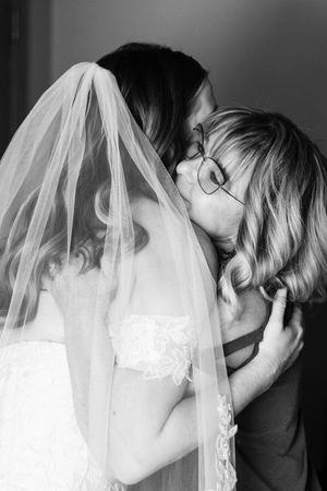Bride in veil hugs a mom with glasses in a heartfelt black-and-white moment