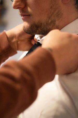 Close up of grooms face as his brother helps him adjust his tie before the ceremony in his childhood home