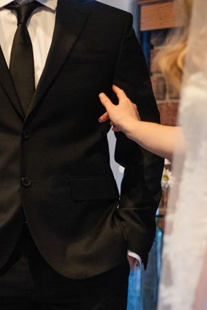 Close up of Brides hand lovingly caresses grooms suit jacket at the alter