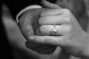 Close up black and white image of groom holding brides hand with ring in the center of the photo