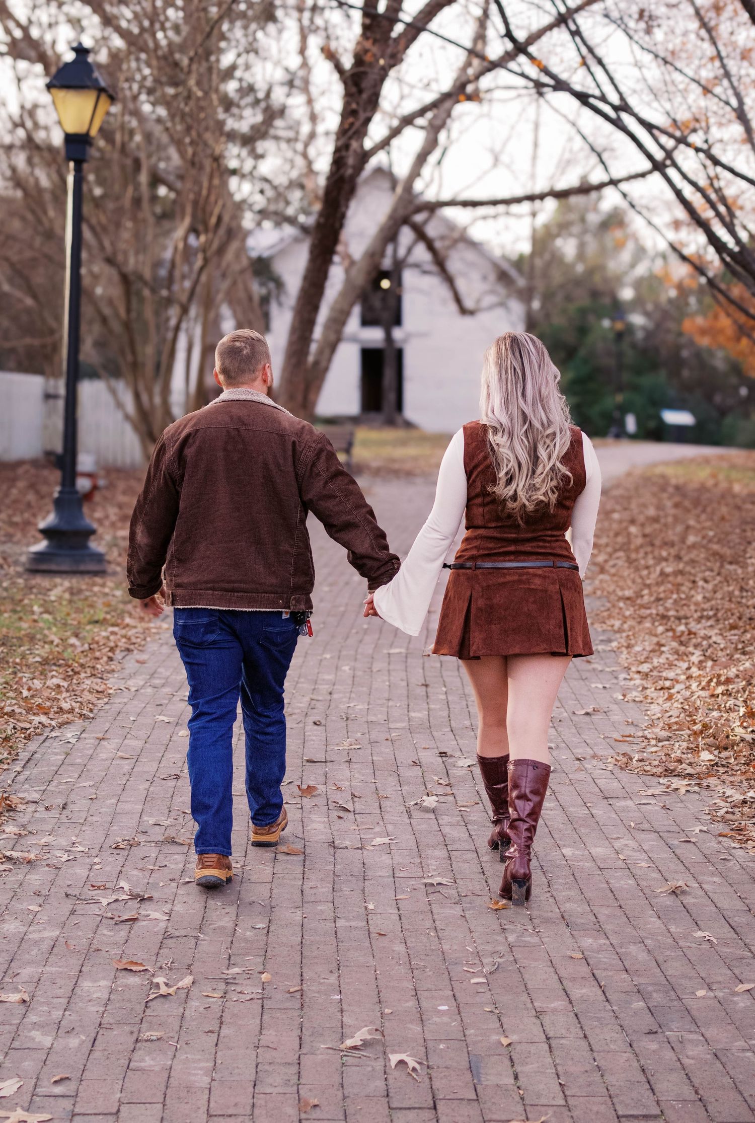 Couple walking hand in hand on a brick path covered in autumn leaves.