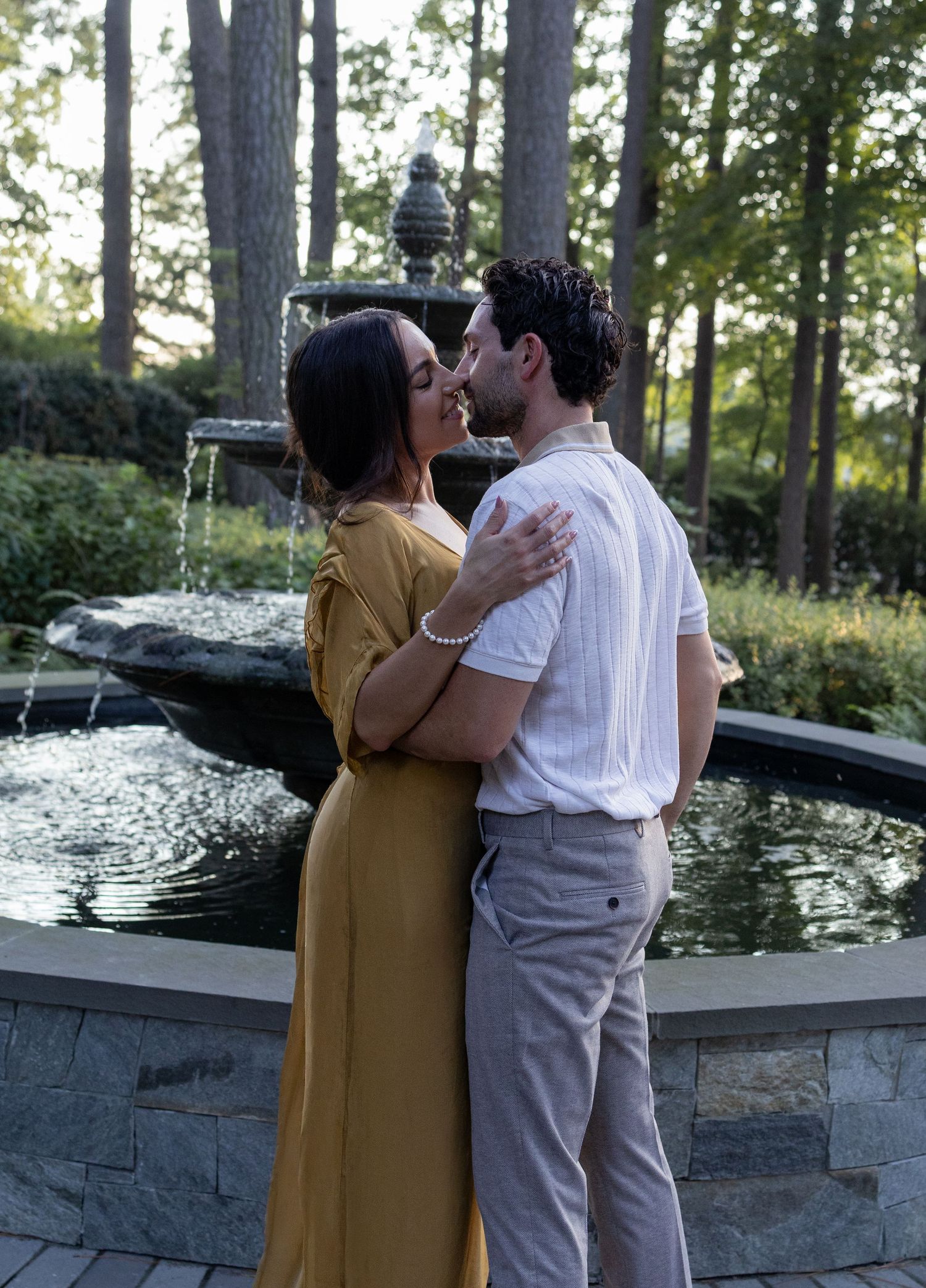 Romantic couple embracing by a garden fountain at sunset.