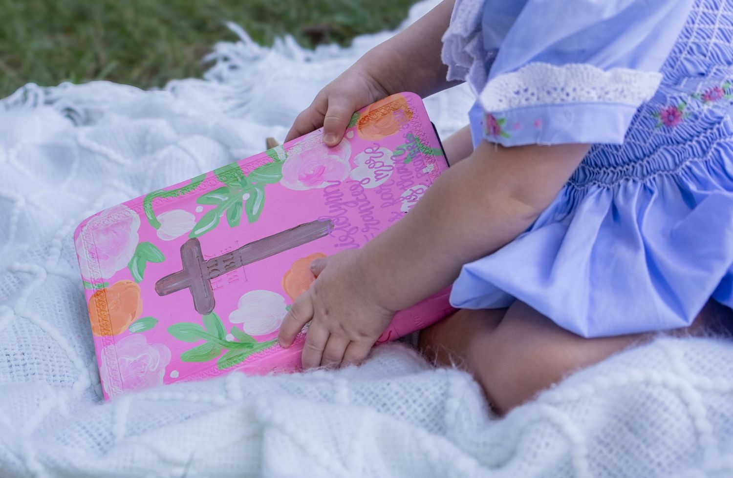 Small hands touching a pink floral book while sitting on white lace fabric.
