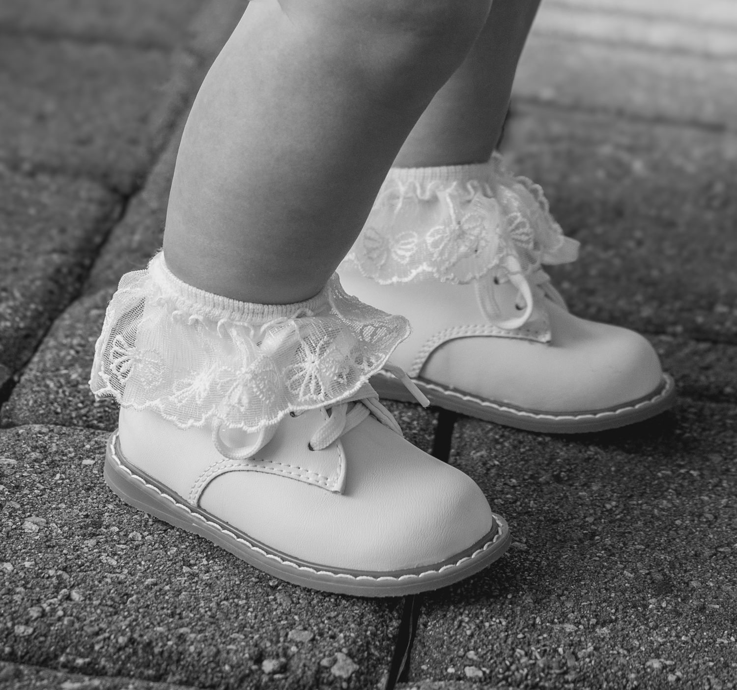 Close-up of tiny white lacy baby shoes on a dark surface.
