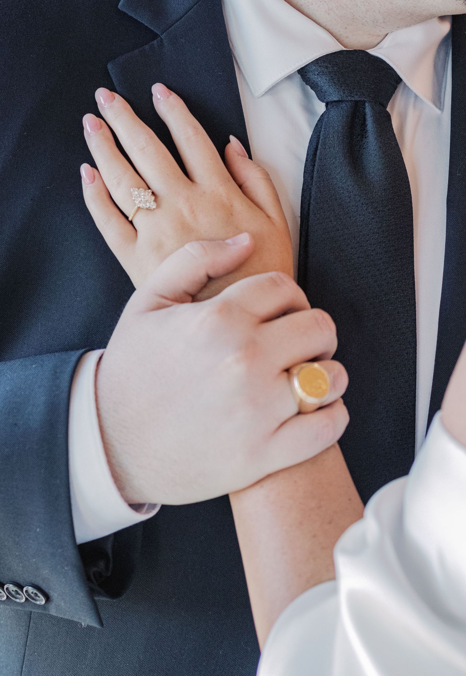 Close-up of hands showing engagement ring and gold signet ring against formal attire.
