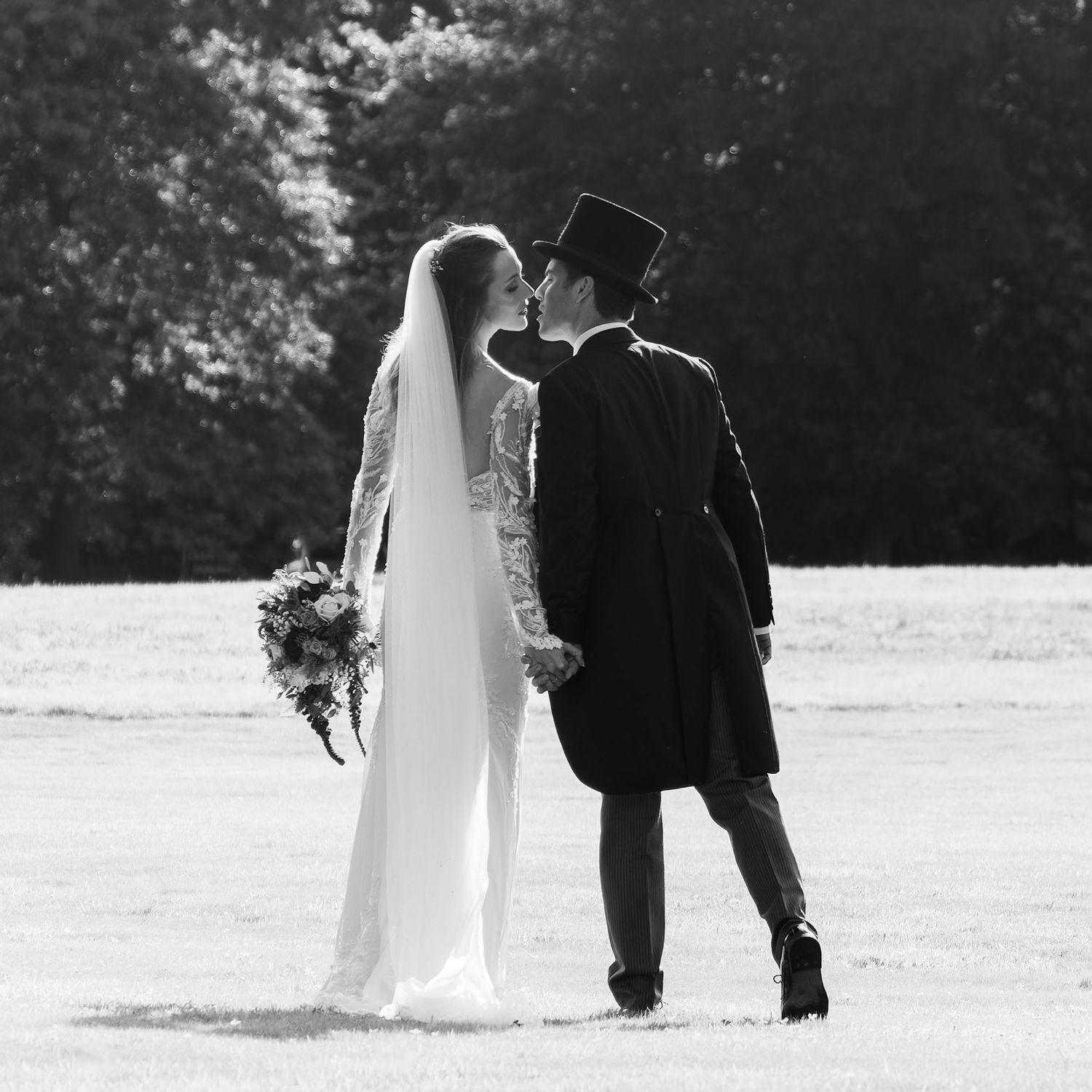 Black and white silhouette of a couple in wedding attire walking together across the lawns at Horsted Place, Sussex
