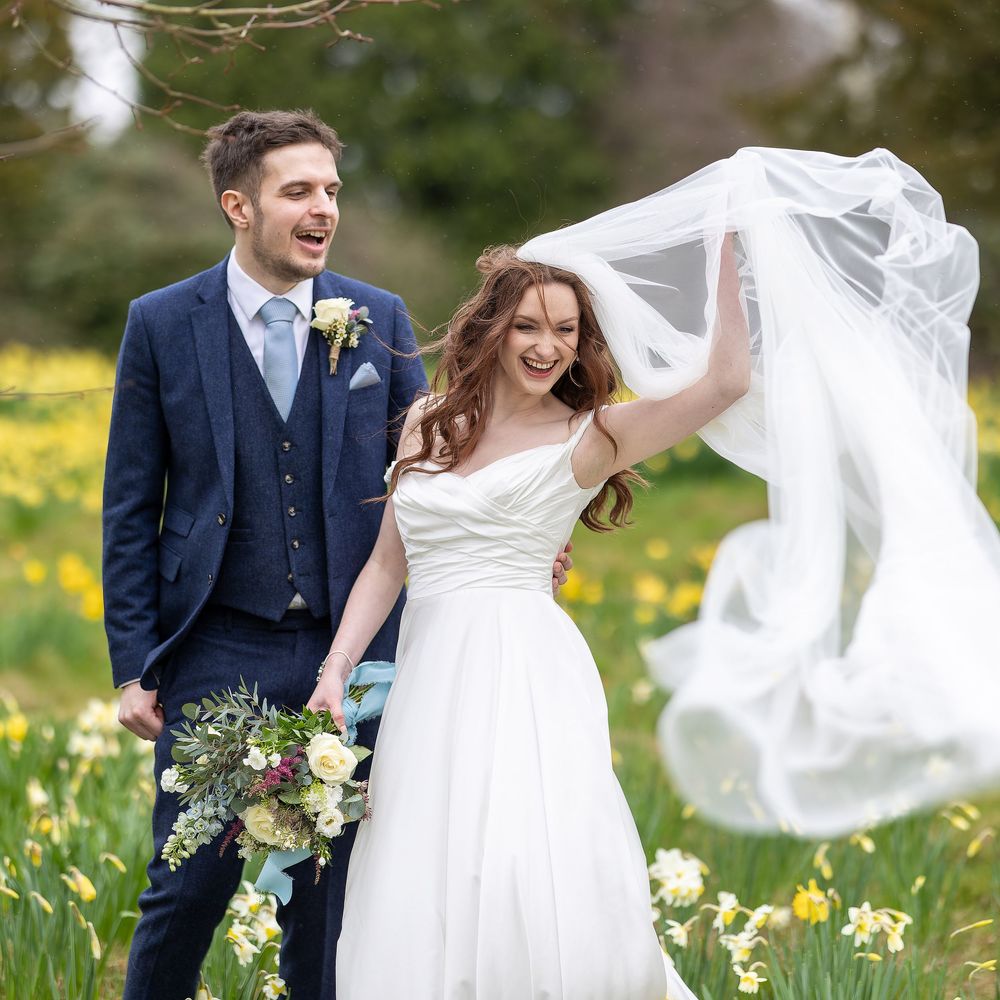 A joyful newlywed couple walks through a springtime meadow filled with blooming daffodils as her veil catches the breeze. Sussex