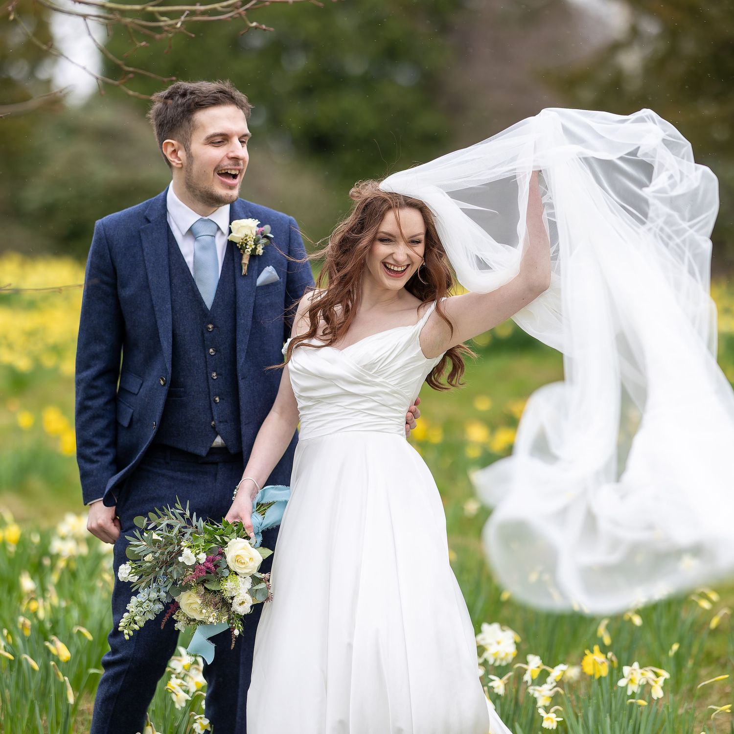 A joyful newlywed couple walks through a springtime meadow filled with blooming daffodils as her veil catches the breeze. Sussex