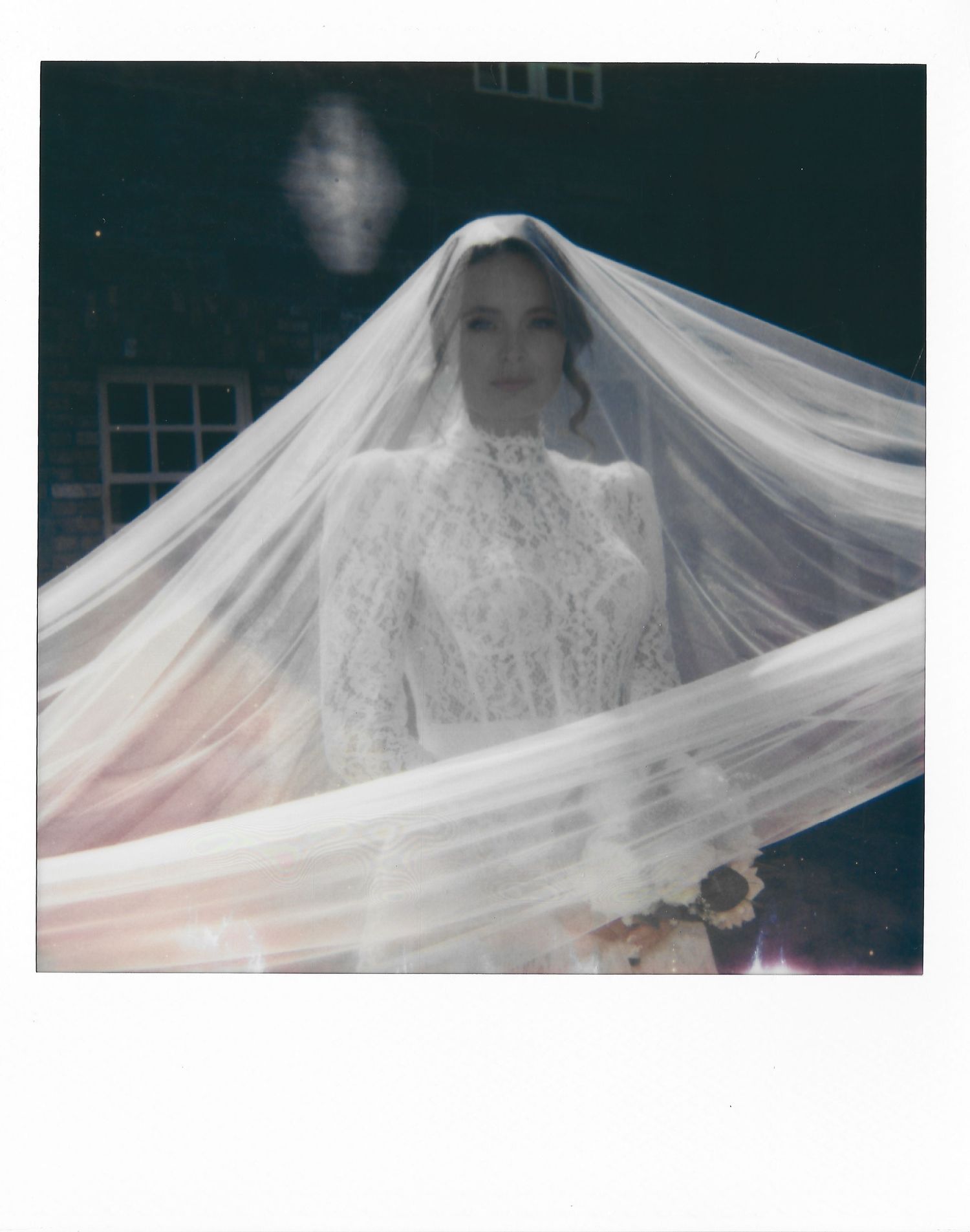 A wedding gown with a flowing white veil photographed in a moody, artistic style against a dark backdrop.