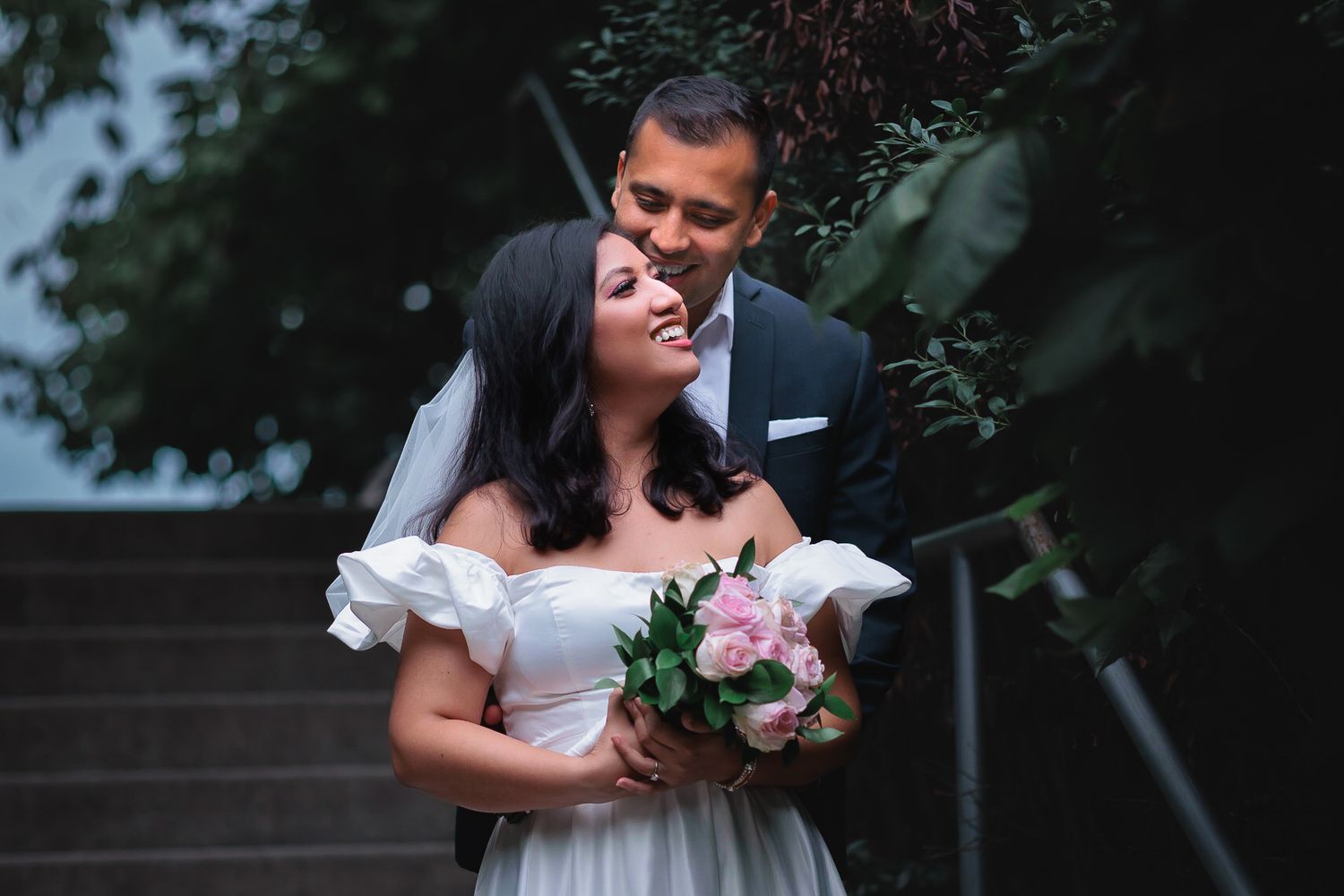 Newlyweds share an intimate moment outdoors surrounded by greenery during their wedding photoshoot.