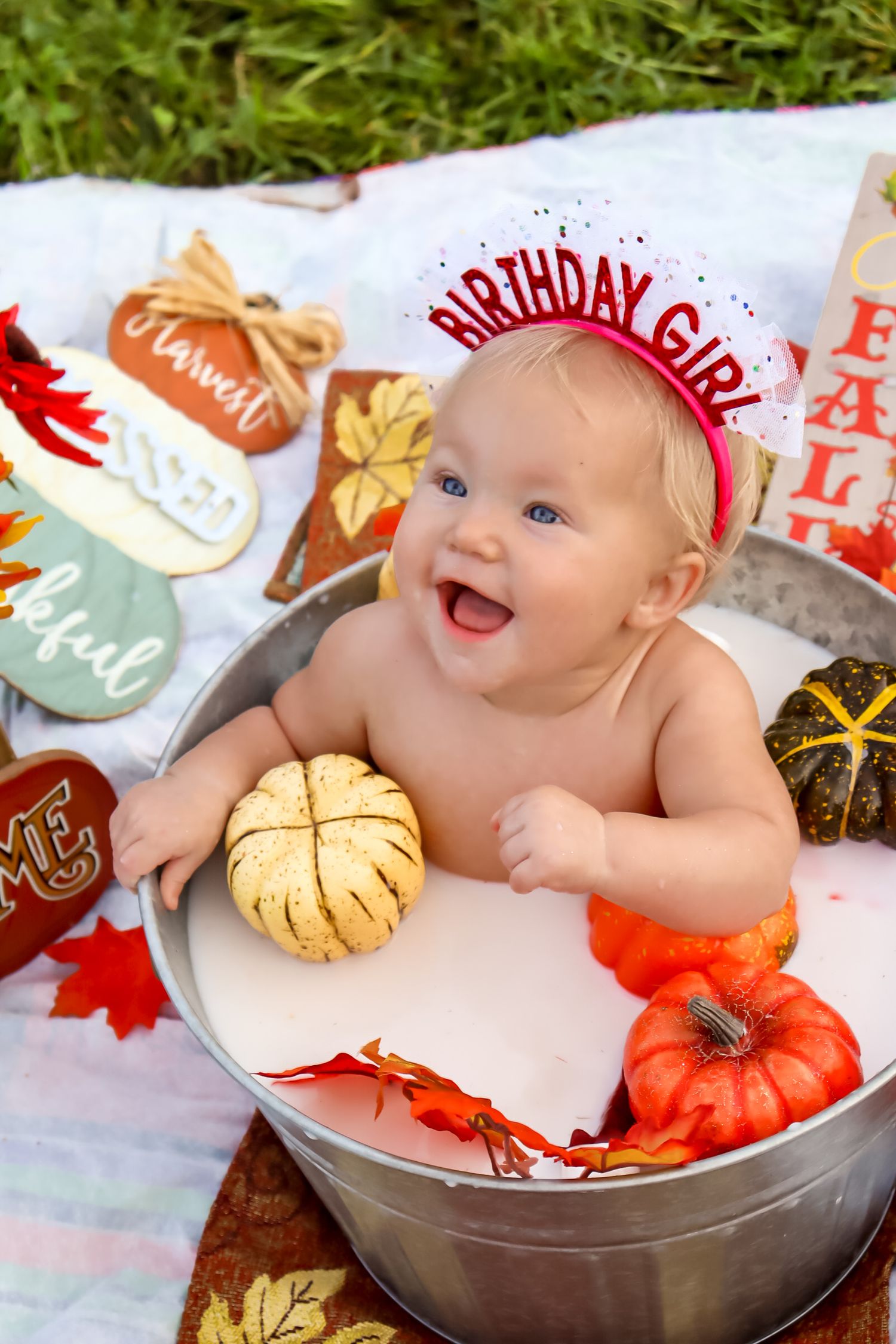 Baby resting in silver bucket with orange pumpkins and autumn leaves for fall themed milestone photoshoot.