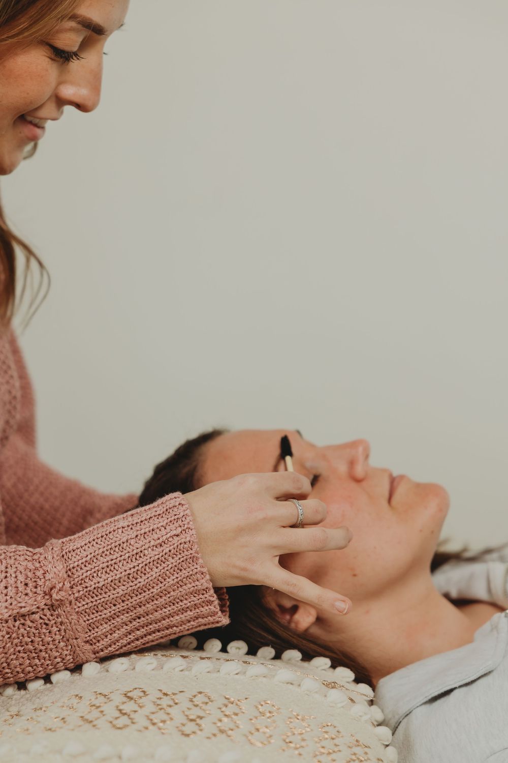 A spa facial treatment being performed on someone laying down on a pillow with a person in pink knit sweater providing care.