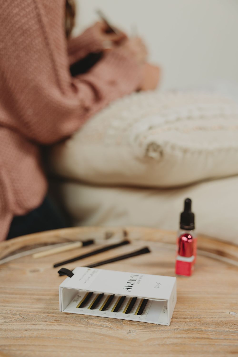 A dropper bottle and product refill cartridges rest on a wooden surface with a cozy blanket and pillow in the background.