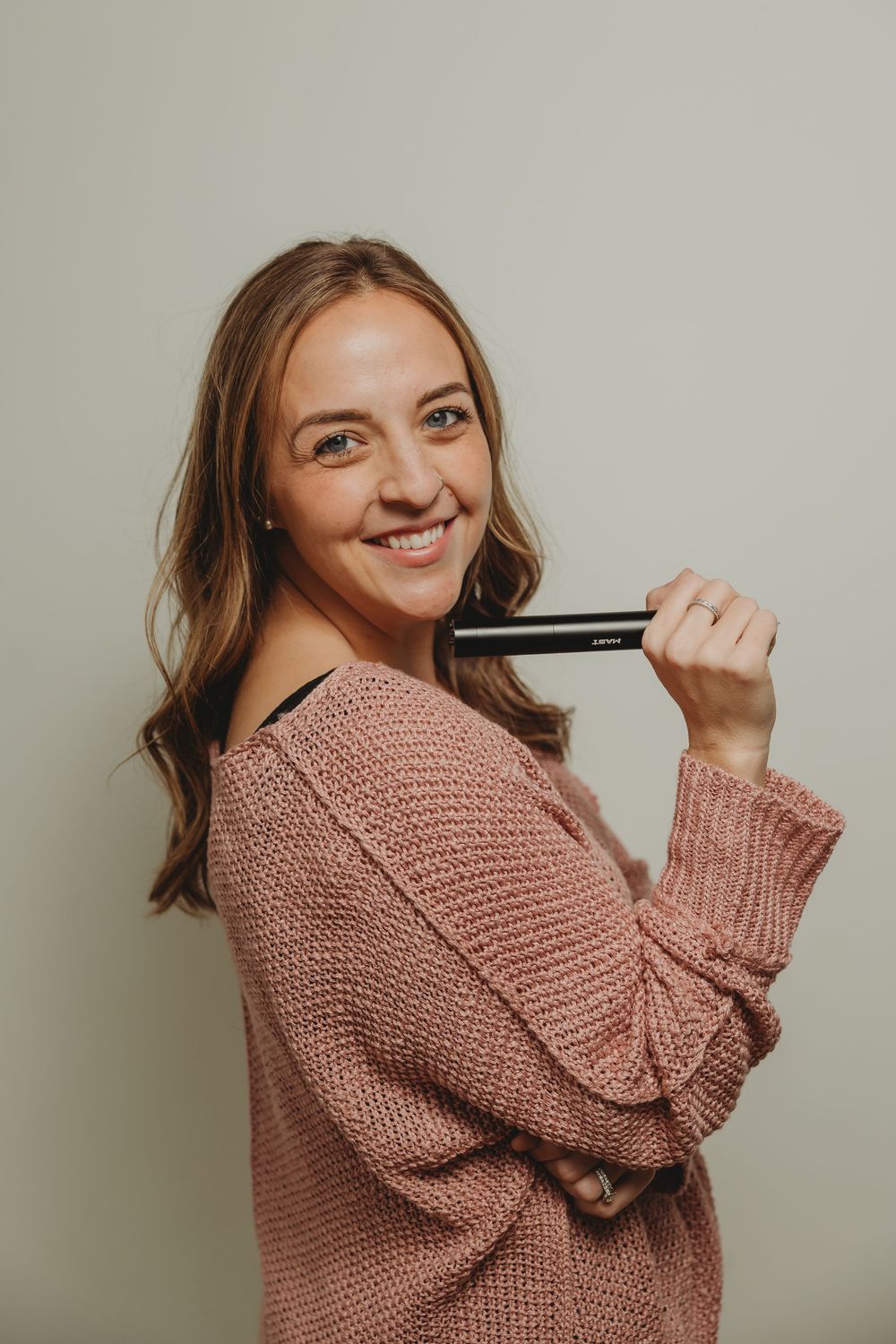 Woman in cozy pink knitted sweater poses playfully against neutral background in photo series.