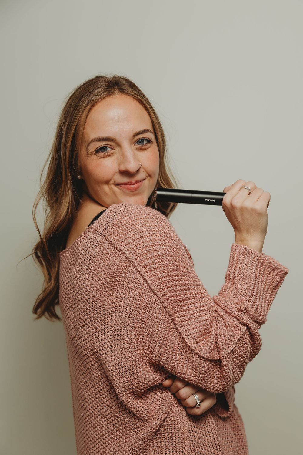 A person wearing a cozy pink knit sweater poses playfully while holding their hair.
