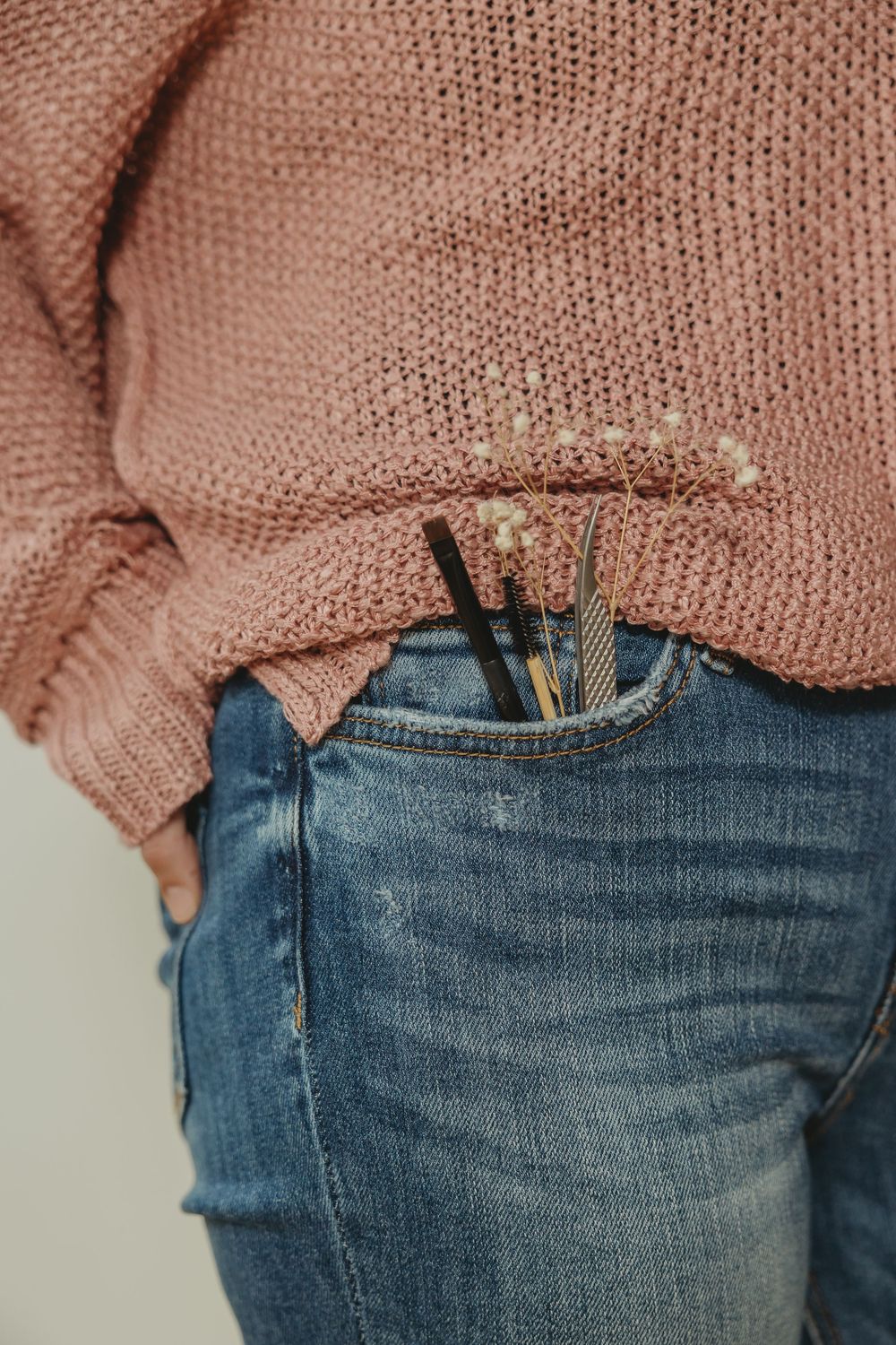 Close-up view of a pink knit sweater tucked into distressed blue denim jeans showing casual styling details.