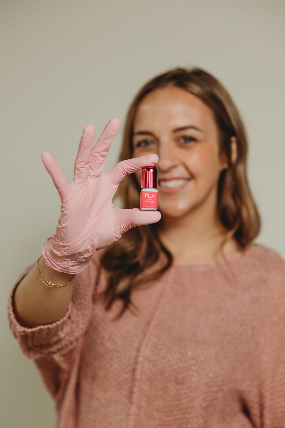 Person wearing pink sweater holds up small bottle of nail polish while wearing protective pink glove.