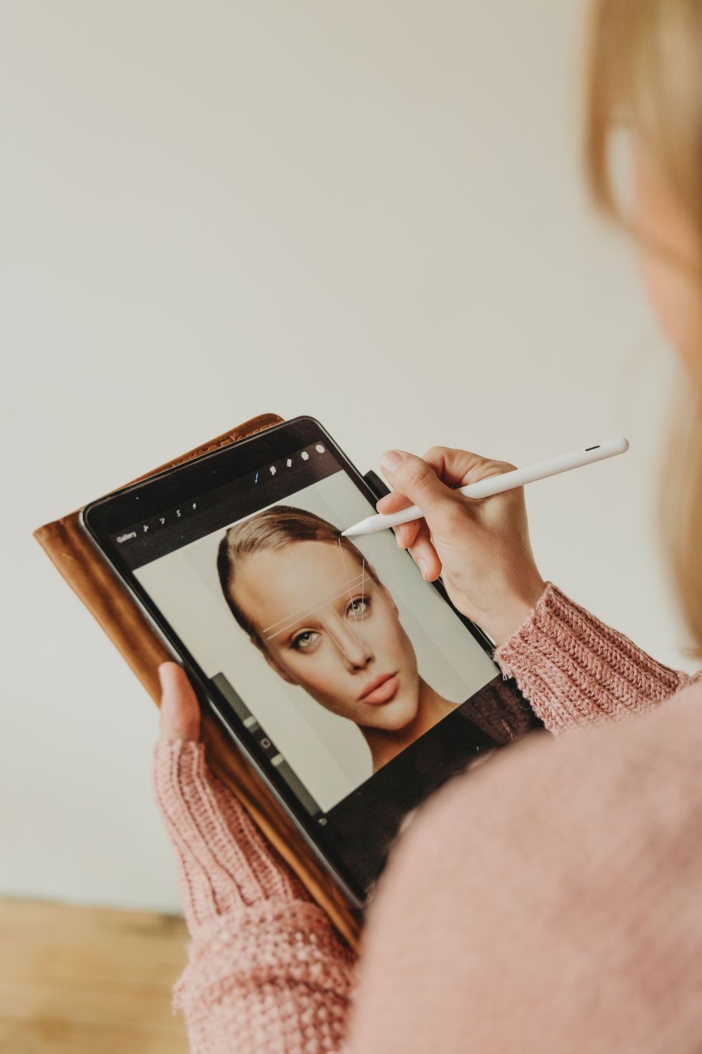 Person wearing a pink knit sweater holds and interacts with a tablet device in a well-lit setting.
