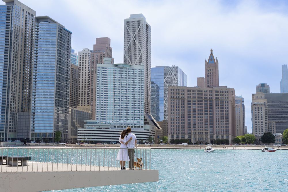 Couple embracing on a pier with Chicago skyline and waterfront skyscrapers in the background on a cloudy day.