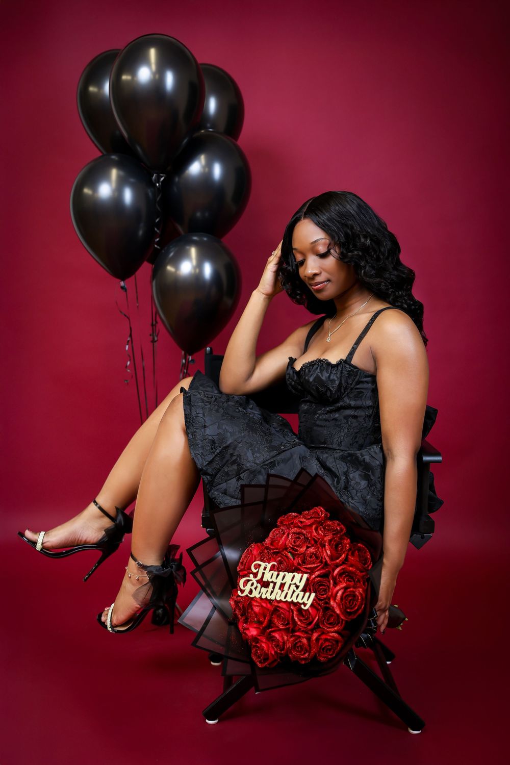 Glamour photo shoot with black balloons and red roses against burgundy background.