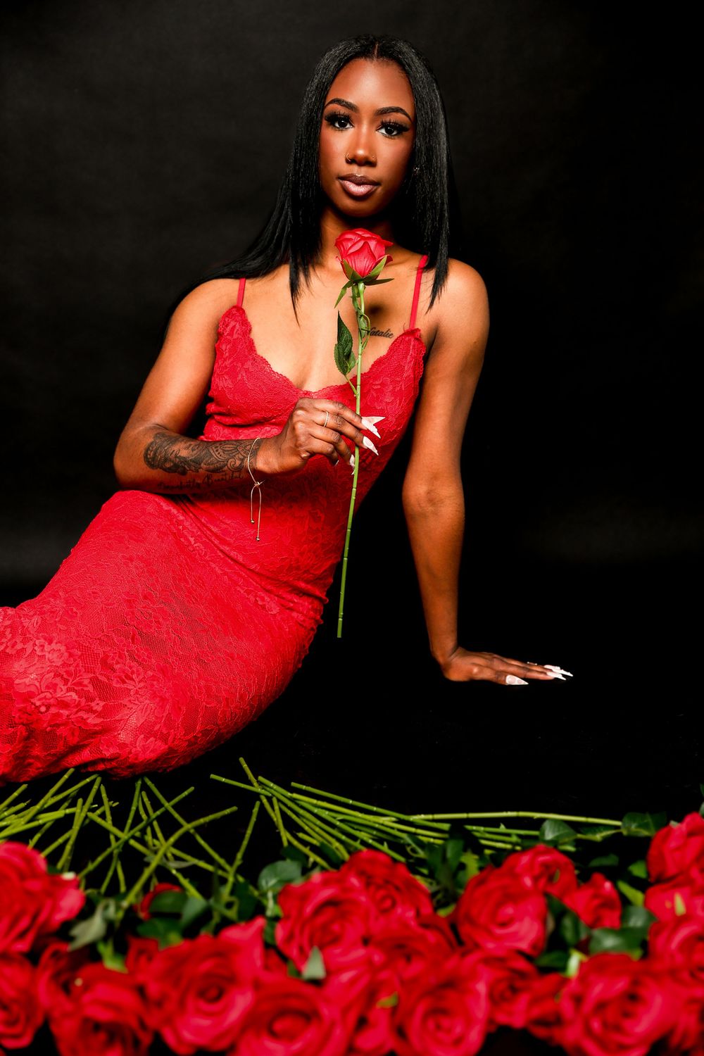 Dramatic fashion shoot with red roses and red lace dress against black backdrop.