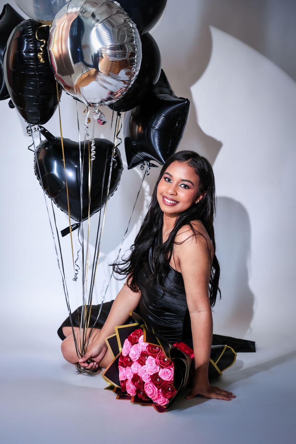 Fashion shoot featuring pink roses and black balloons against white studio backdrop.