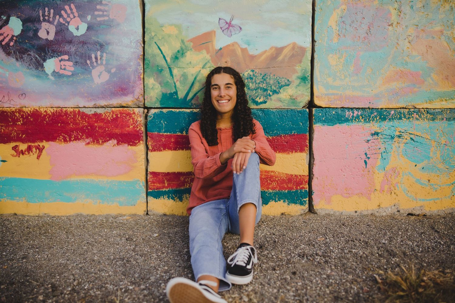 Someone sits casually against a vibrant painted wall featuring pink and orange stripes with whimsical artwork in the background.