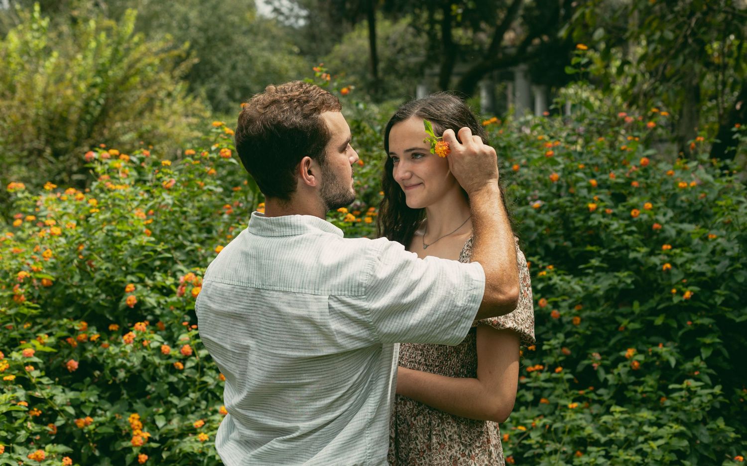 A romantic scene unfolds in a garden filled with yellow flowers and greenery.