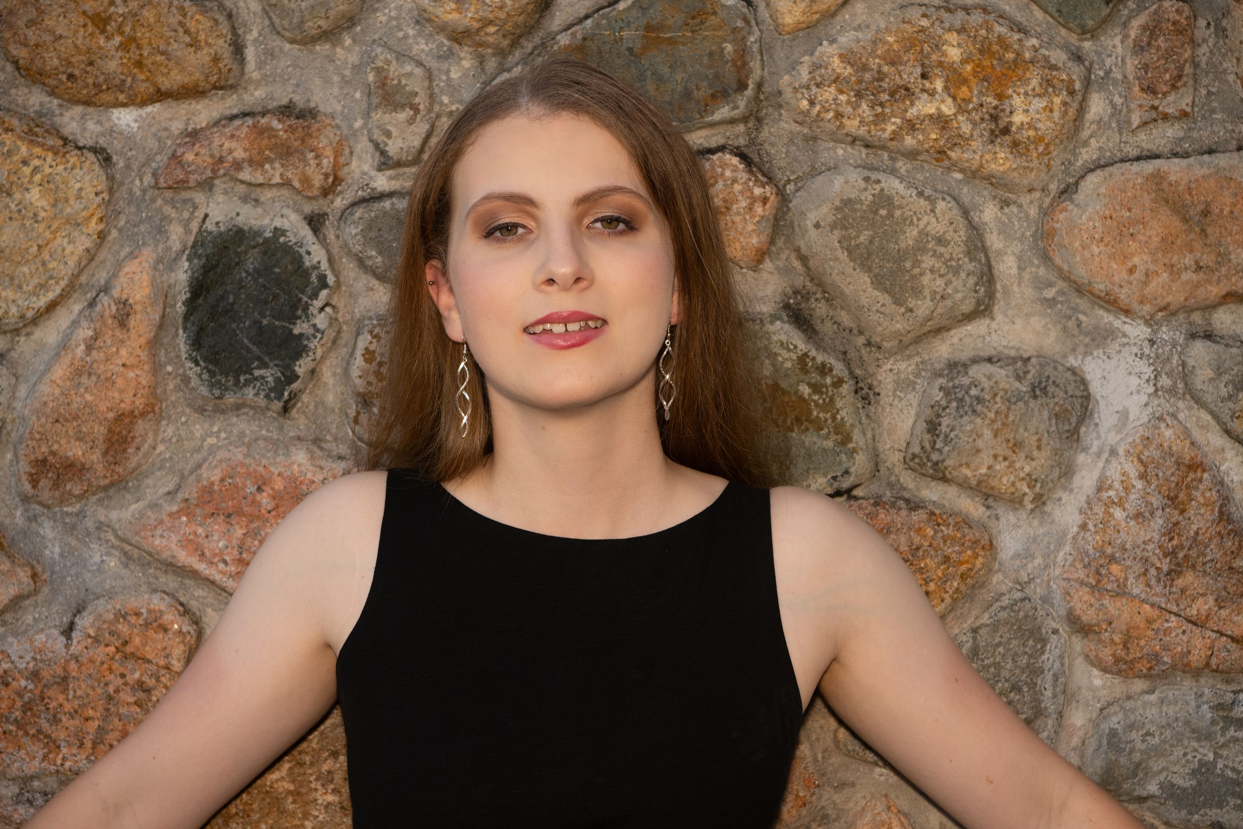 Portrait against stone wall wearing black sleeveless dress.