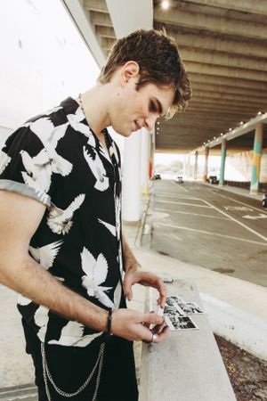 Person in black and white dove print shirt looking down while standing in a covered parking area.