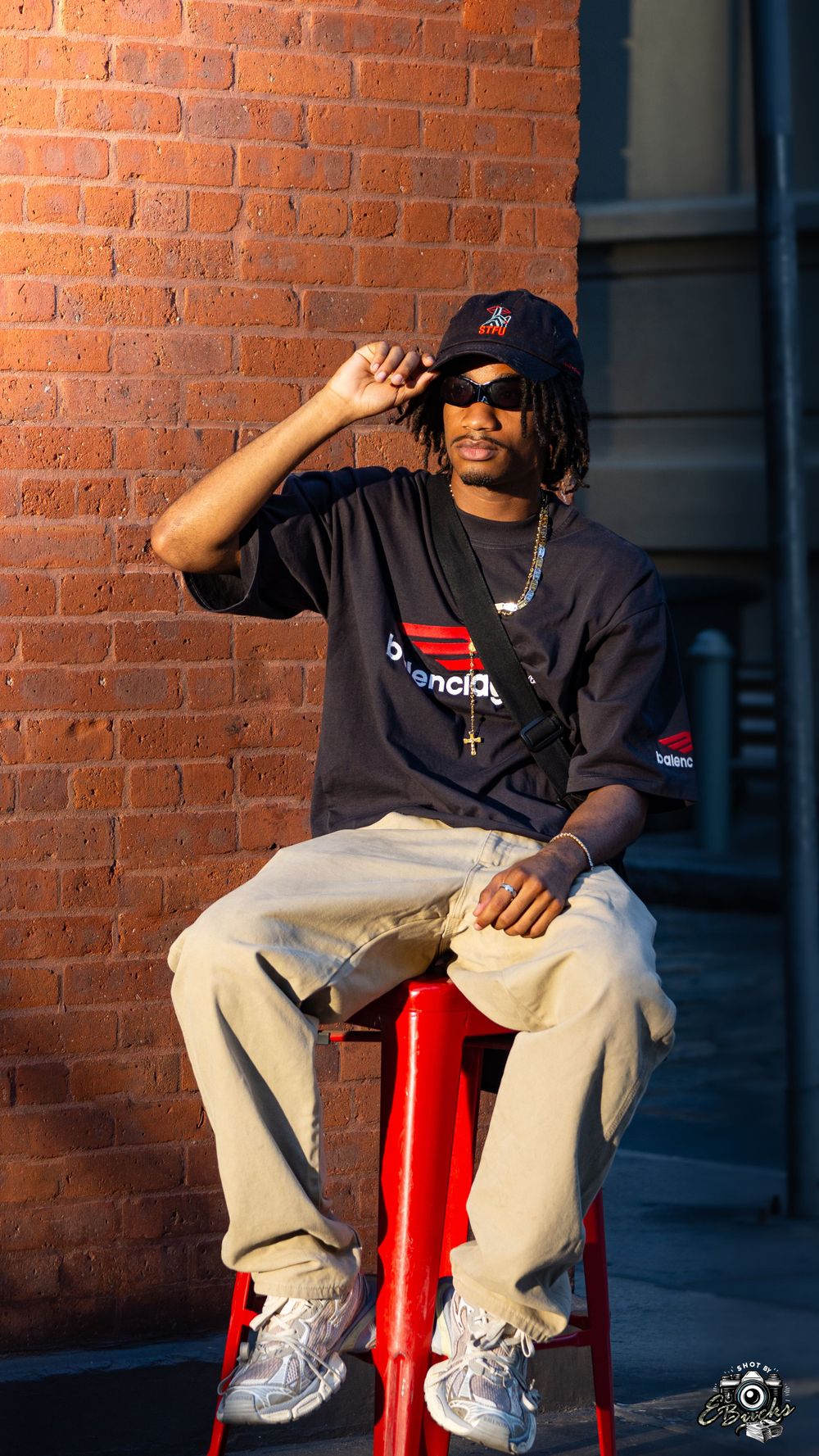 Urban fashion portrait against brick wall with red metal stool and sunglasses.