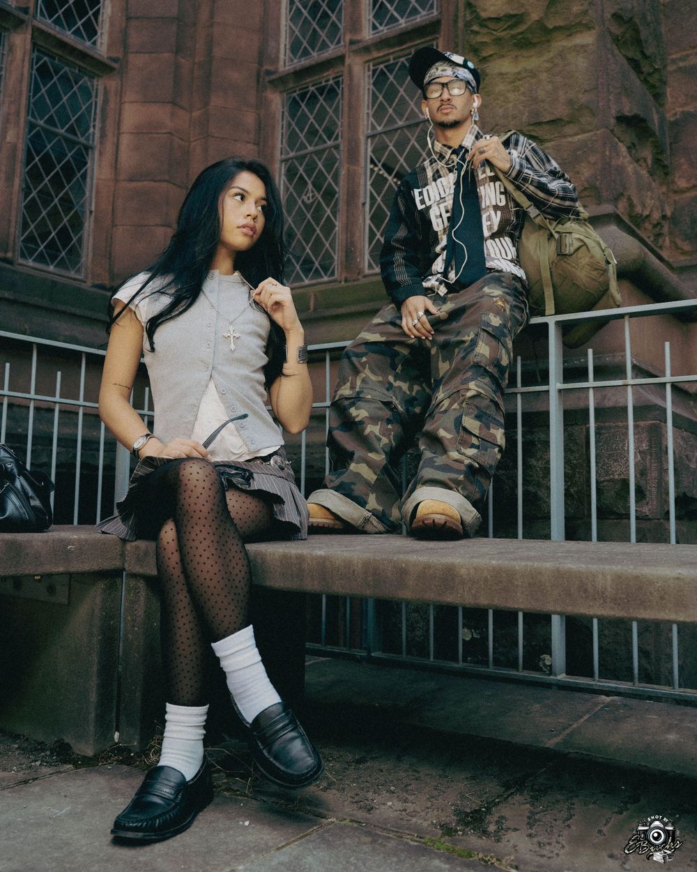 Gothic-style fashion shoot featuring a model in fishnet stockings and black boots posing against a stone building exterior.