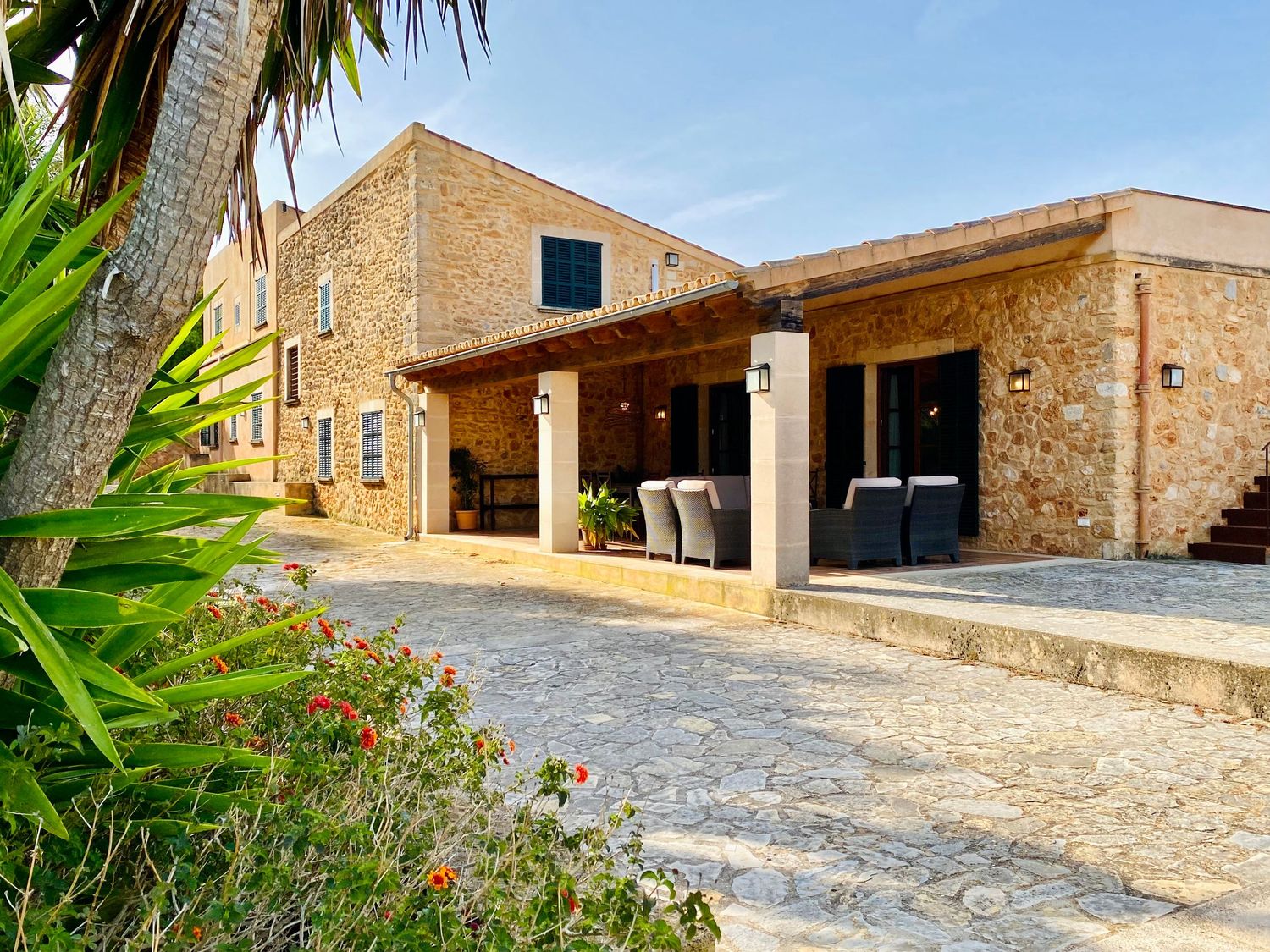 Mediterranean stone villa with covered porch and palm trees in a rustic setting.