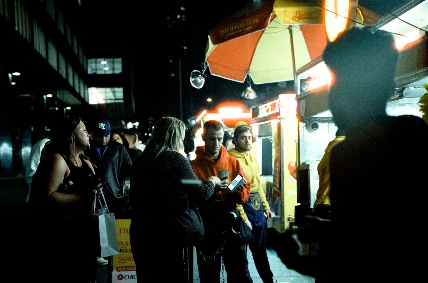 Street food vendor with umbrella serving customers at night.