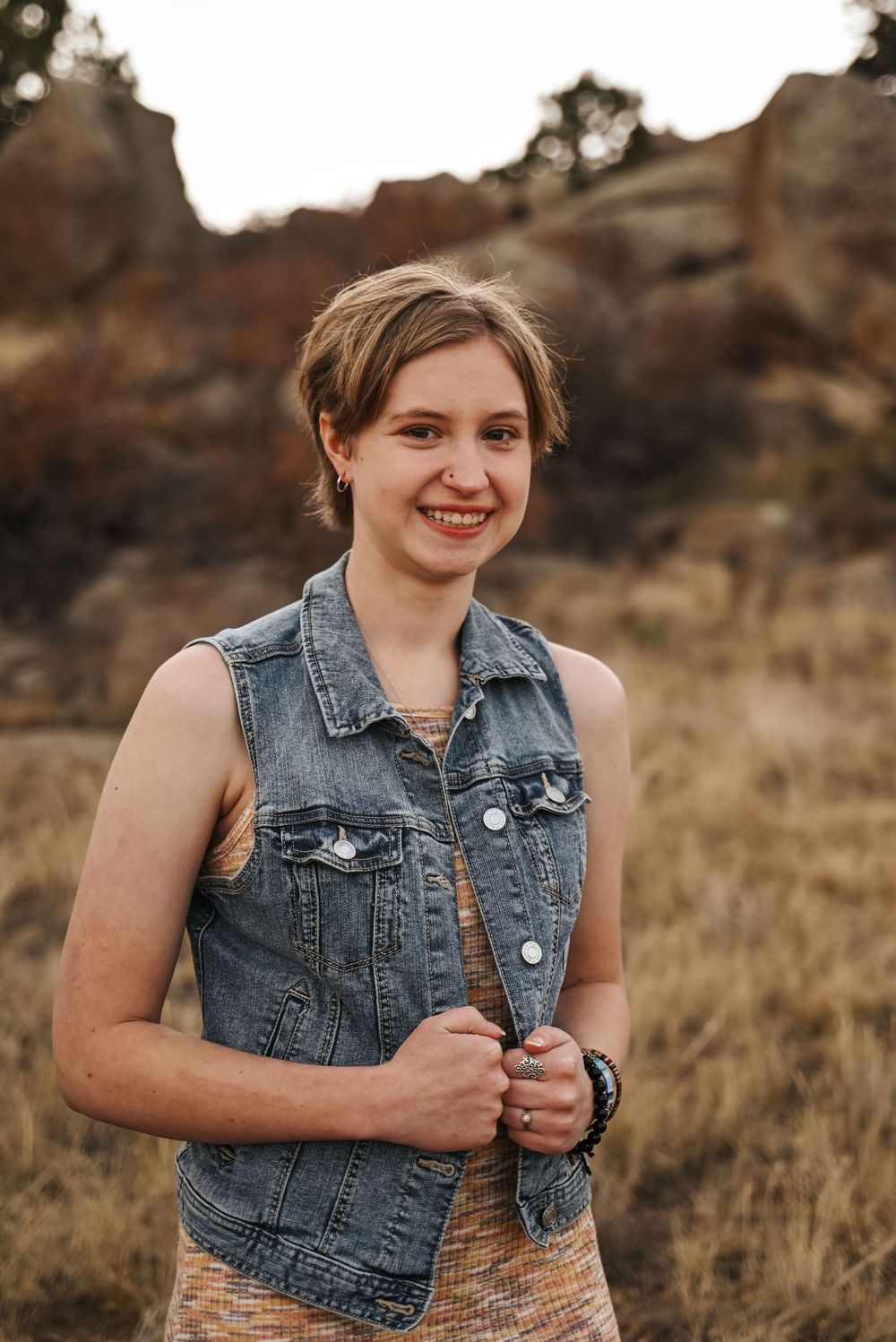 Portrait session featuring denim vest against rocky natural backdrop at sunset.