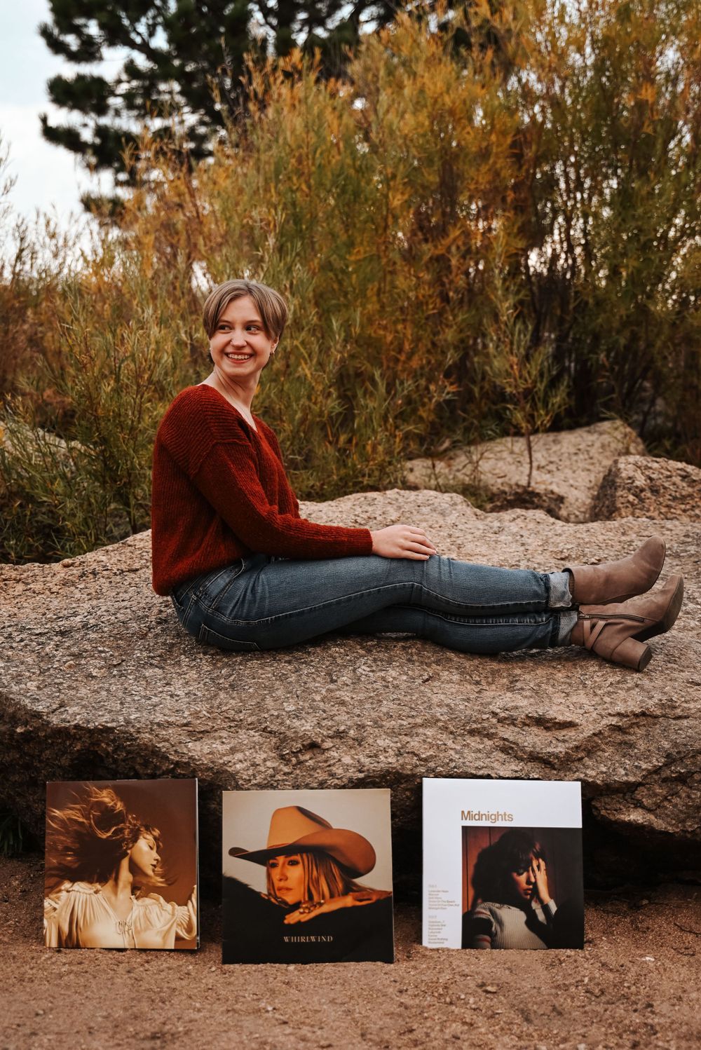 Casual portrait with vinyl records displayed against rocky outdoor backdrop.