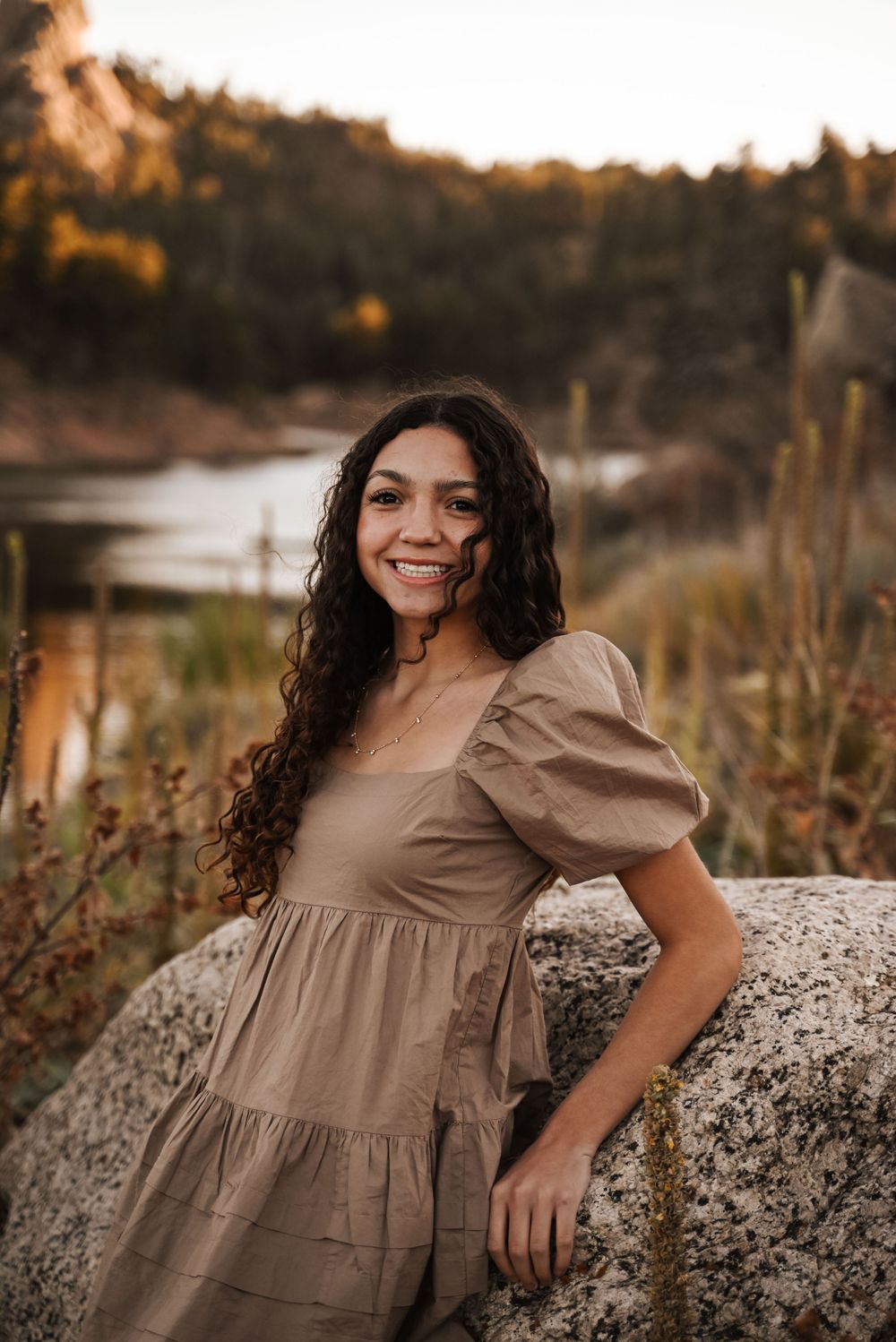 A person in a brown prairie dress poses on rocky terrain during sunset.