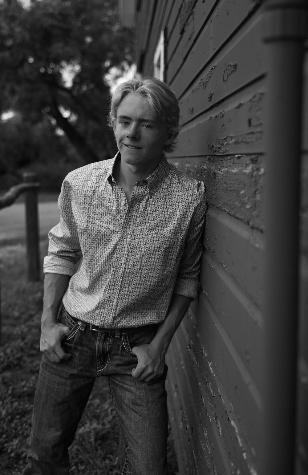 Black and white portrait of person in checkered shirt leaning against weathered wall.