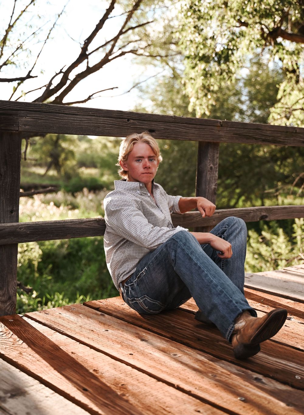 Casual portrait of person relaxing on wooden deck bench in natural setting.