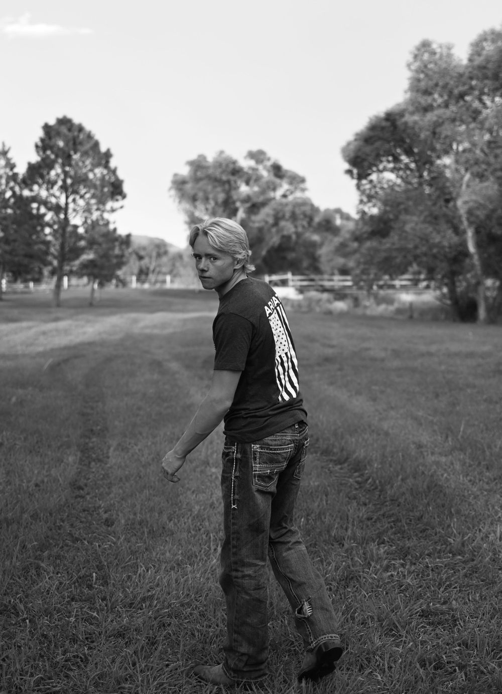 Black and white image of person walking through grassy park area.