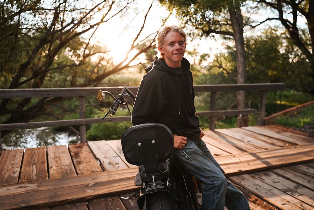 Person sitting with guitar case on wooden bridge at sunset.
