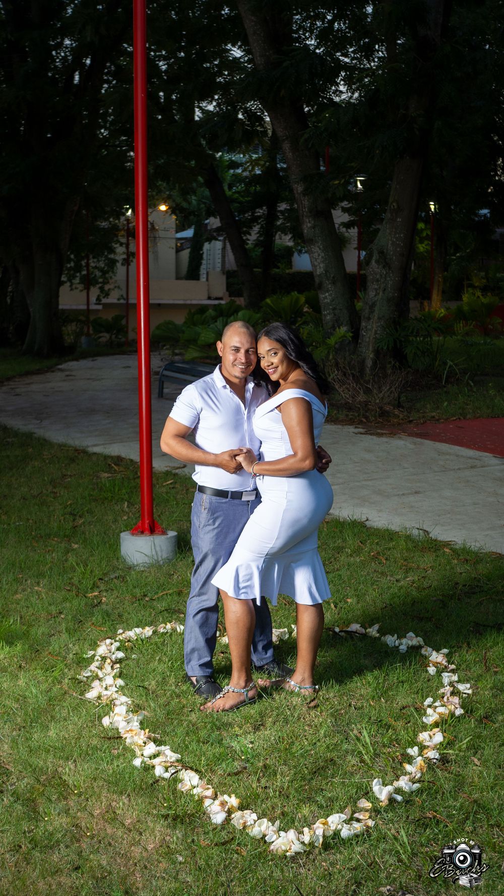 Happy couple embracing inside heart shape made of white flowers outdoors.