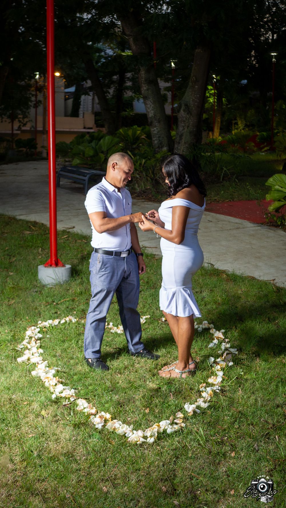 Couple getting engaged in heart made of flowers on grass during sunset.