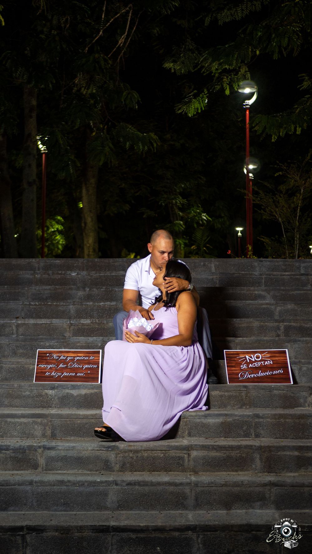 Couple sharing intimate moment on concrete steps at night with signs.