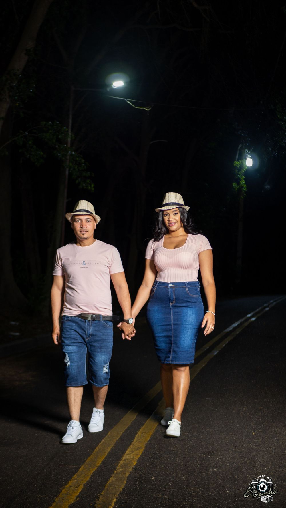 Couple in matching pink outfits and hats walking together at night under streetlights.